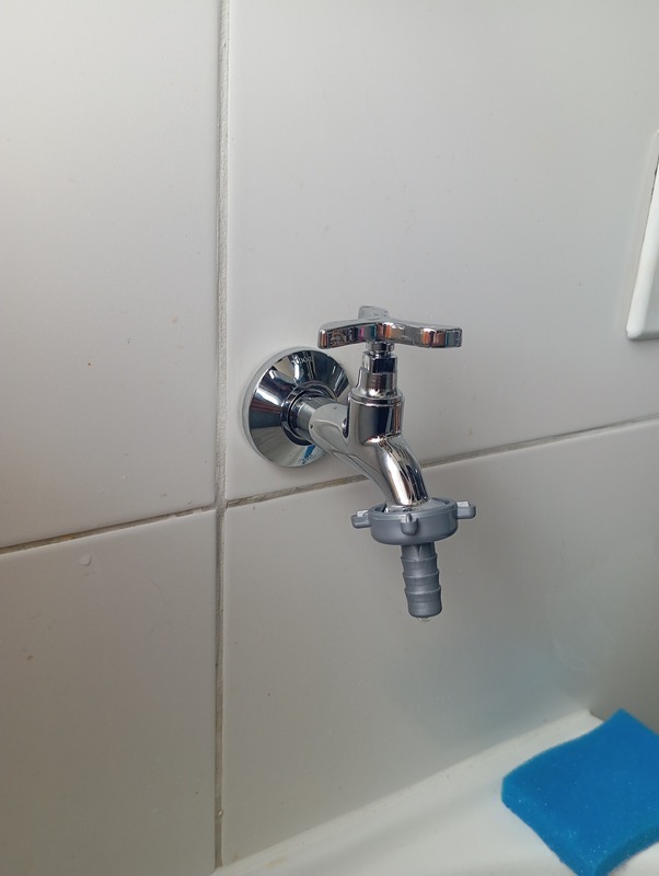 Torneira cromada de parede em área de serviço
